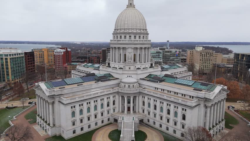 Scenic aerial view of Madison’s city center, featuring the Wisconsin State Capitol and nearby lakes under a cloudy sky.