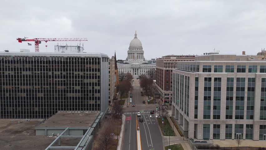 Drone view of downtown Madison with the Wisconsin State Capitol as the central landmark, framed by urban streets and waterways.