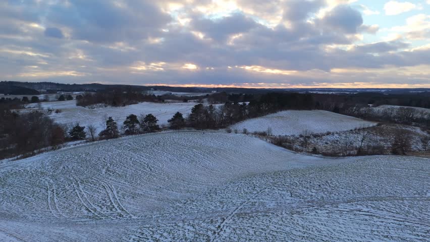 Drone perspective of Wisconsin’s countryside in winter, where rolling land and scattered forests lie beneath a smooth layer of snow.