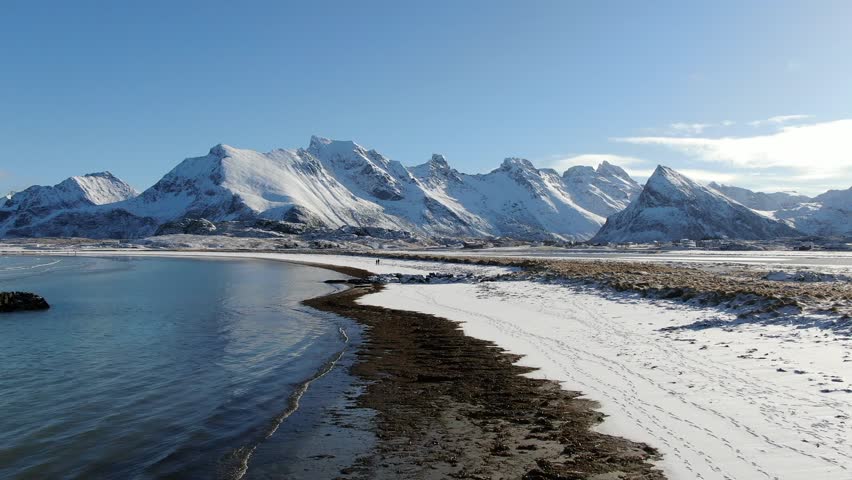 Aerial view of a snow-covered white sand beach near Fredvang and Ramberg, where the winter Lofoten landscape glows under a steel-blue sky in crisp Arctic light.