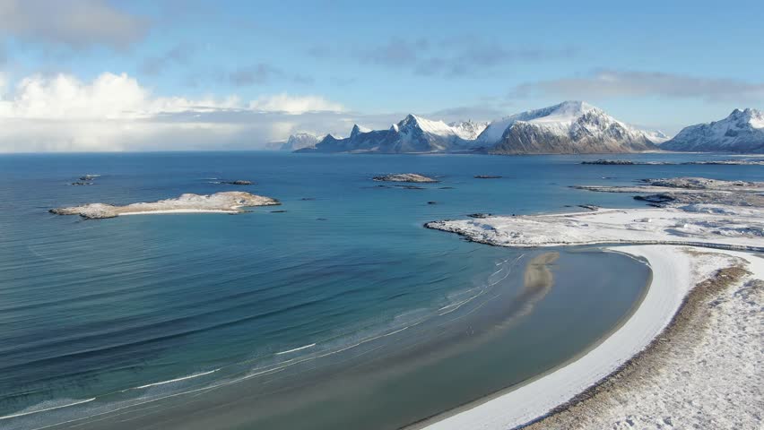 Aerial view of a snow-covered white sand beach near Fredvang and Ramberg, where the winter Lofoten landscape glows under a steel-blue sky in crisp Arctic light.