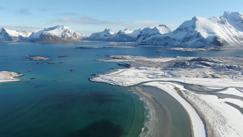 Aerial view of a snow-covered white sand beach near Fredvang and Ramberg, where the winter Lofoten landscape glows under a steel-blue sky in crisp Arctic light.
