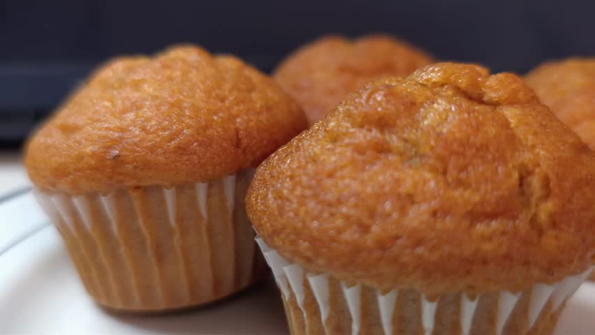Close-up side view of delicious golden brown muffins in white paper liners on a plate.