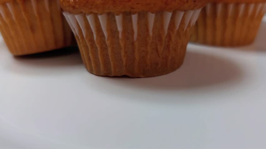Camera tilting up to reveal delicious golden muffins in paper liners on a white surface.
