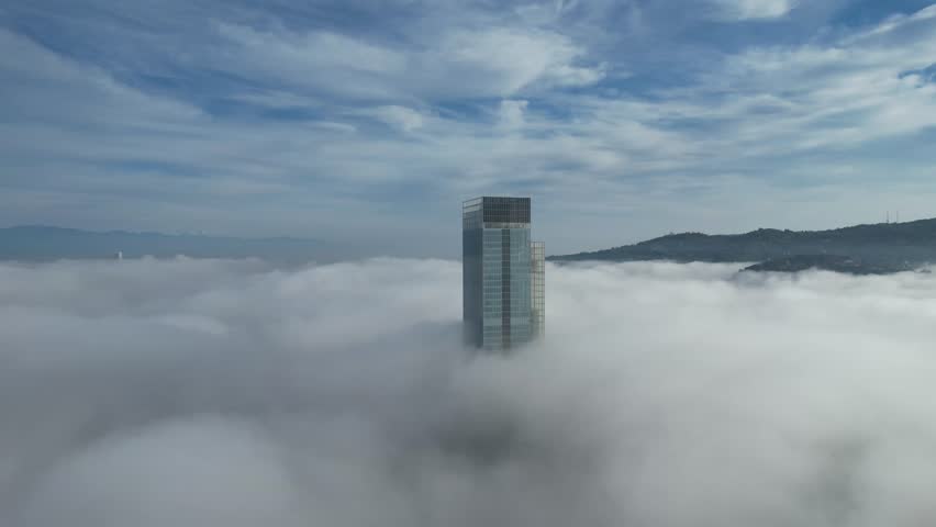 Aerial view of a solitary skyscraper piercing through a sea of fluffy white clouds, with mountains in the distance, Torino, Piemonte, Italy.