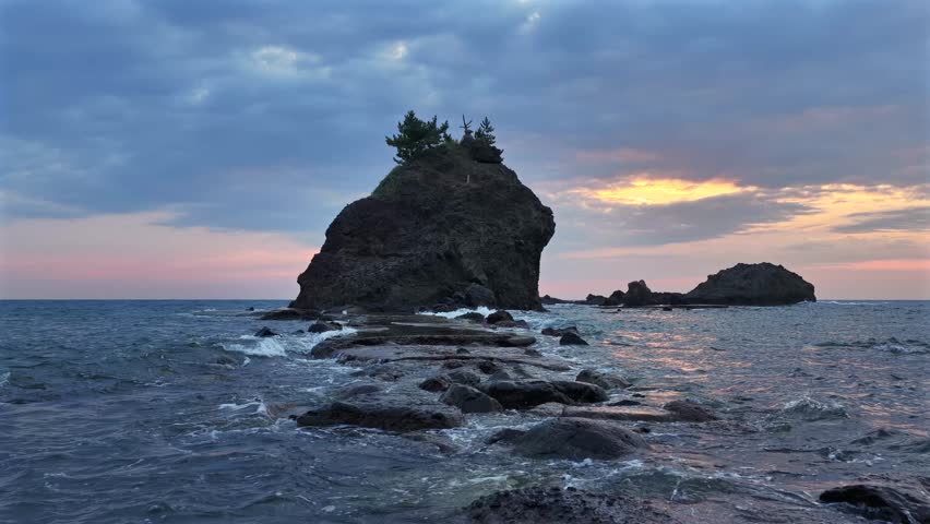 Aerial view of dramatic rock formations meeting the sea under a cloudy sky reflecting light off the water, Sendai, Miyagi, Japan.