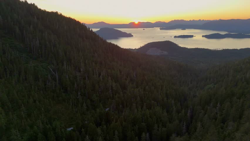 Aerial view of islands surrounded by water meeting the lush green mountain ranges under the warm glow of the setting sun, Sitka, Alaska, United States.