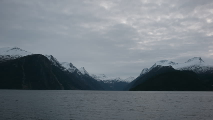 Panoramic shot of an entrance to a fjord in Norway with tall mountains and snow covering the peaks on a cold winter day