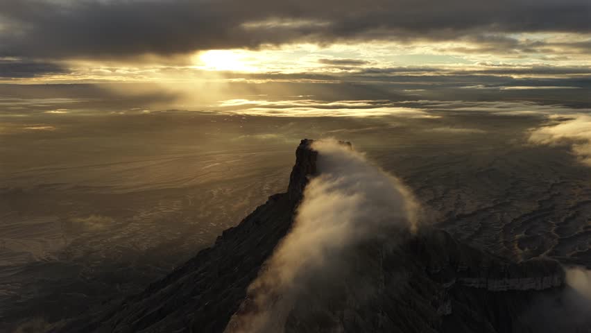Aerial view of the majestic Mount Hillers shrouded in ethereal clouds, contrasting with the rugged Utah landscape and the golden sunlight, Hanksville, Utah, United States.
