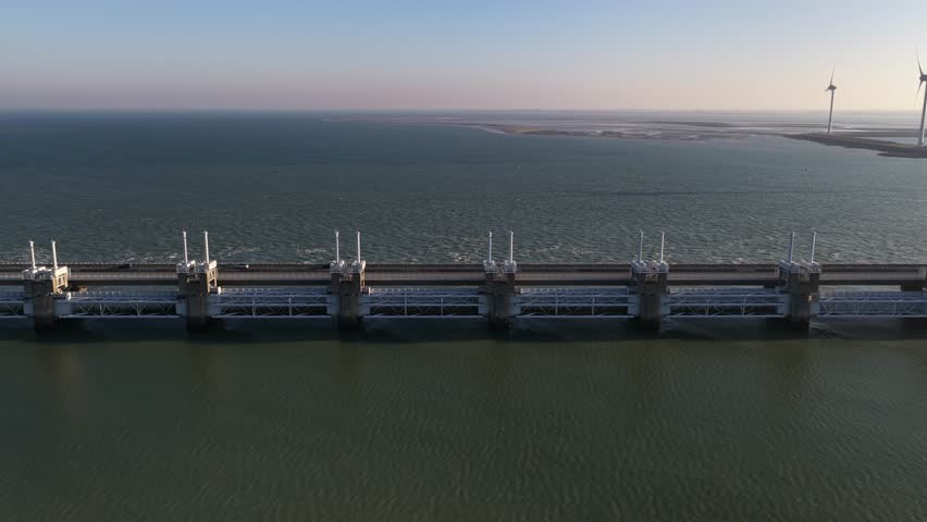 Aerial view of the imposing Oosterscheldekering barrier stretching across the waters with wind turbines in the background, Vrouwenpolder, Zeeland, Netherlands.