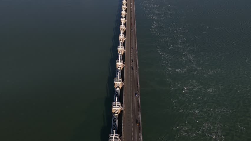 Aerial view of the impressive Eastern Scheldt storm surge barrier cutting through the waters with windmills, Vrouwenpolder, Zeeland, Netherlands.