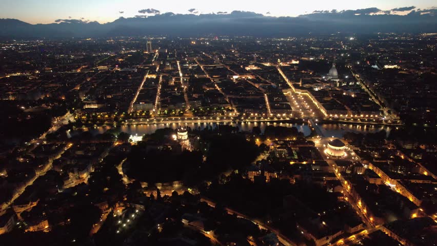 Aerial view of the illuminated cityscape featuring Mole Antonelliana at dusk, with lights reflecting on the river, Torino, Piemonte, Italy.