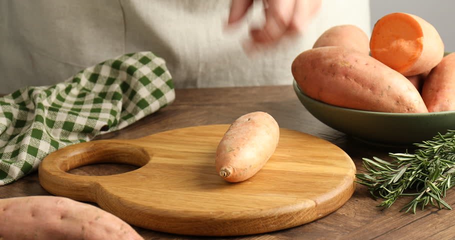 Woman peeling sweet potato at wooden table, closeup