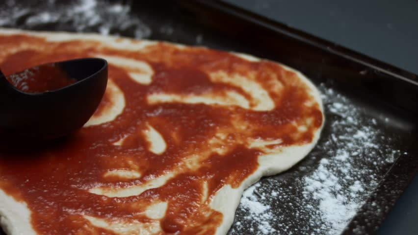 Spreading tomato sauce over the heart shaped pizza dough