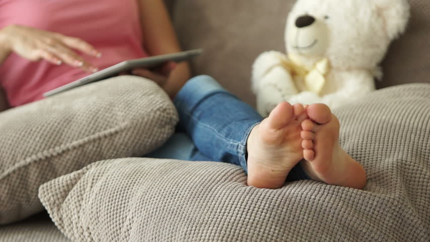 Girl sits on sofa with tablet. Close-up of the feet

