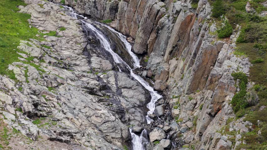 A small mountain waterfall falls from a cliff in the middle of a beautiful valley on a clear sunny day