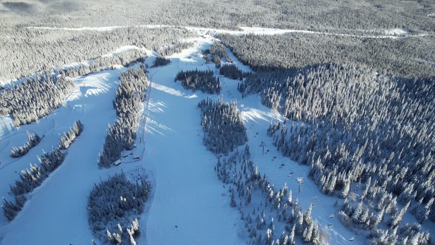 A dynamic moving aerial shot tracks forward, following the path of a chairlift on the snowy slopes of Mount Sima ski resort near Whitehorse, Yukon