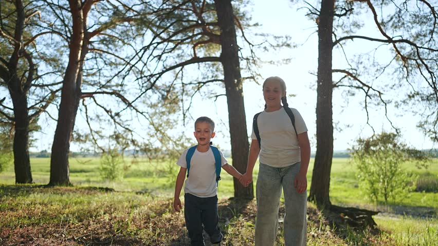 Boy smiles holding sister hand. Girl leads child brother through tall trees. Forest walk brings joy. Happy boy laughs with sister. Child enjoys playful walk with girl. Forest trees frame joyful child.