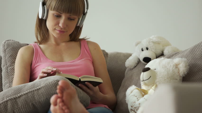 Girl reading book and listening music. She strokes teddy bear
