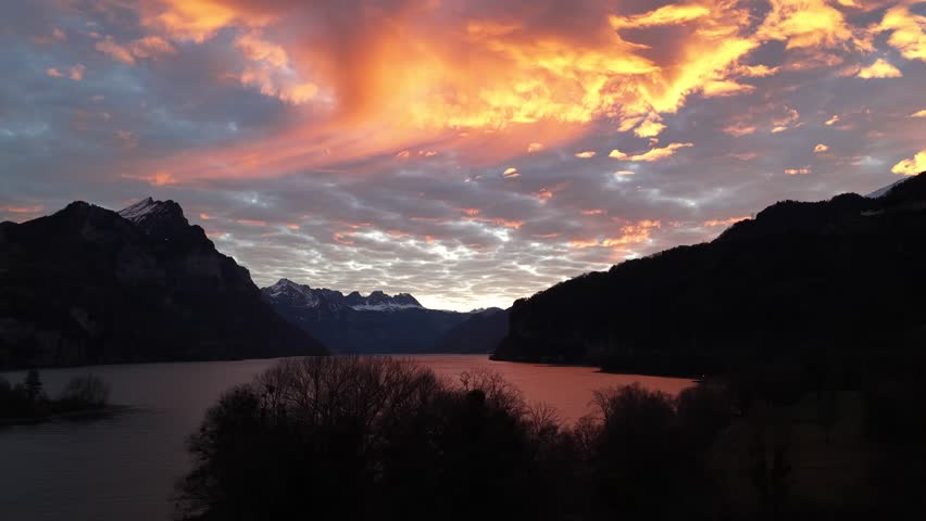 Warm sunset clouds reflecting over a calm alpine lake surrounded by dark mountain silhouettes.