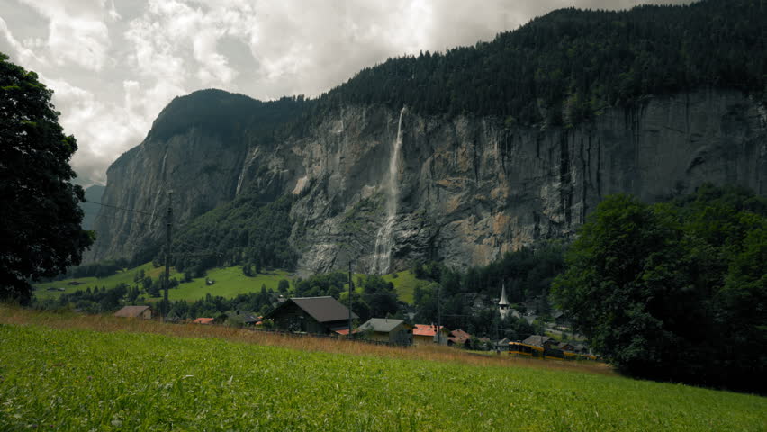 Scenic train climbing through the Lauterbrunnen Valley beneath towering cliffs and waterfall in the Swiss Alps countryside