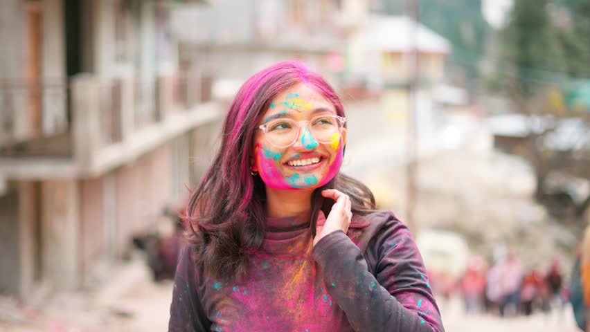 4K Portrait of Indian woman during Holi festival. Face covered with powdered colours during Holi Festival in Sangla, Himachal Pradesh, India. Hindu woman celebrating. Tourists seeking cultural experiences.