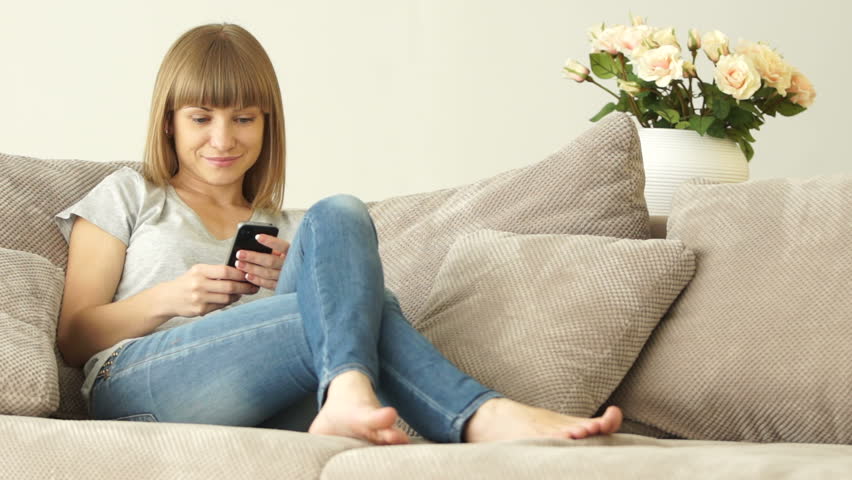 Girl with the phone sitting on a couch and smiling
