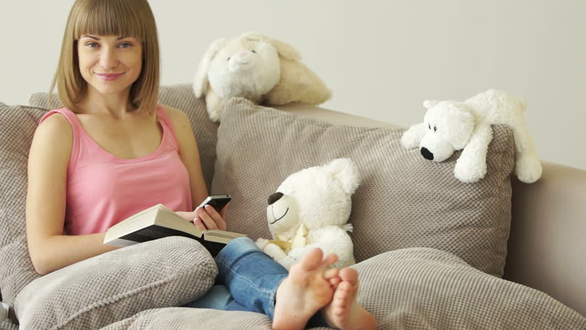 Girl sitting on the couch with book and telephone
