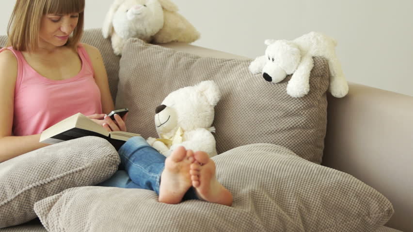 Girl resting on the couch and dials the number. Around stuffed toys
