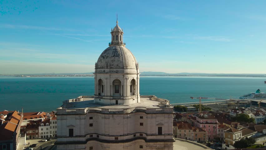 Aerial orbit of the Lisbon National Pantheon showing its white dome above traditional rooftops with the Tagus River in the background on a sunny clear day