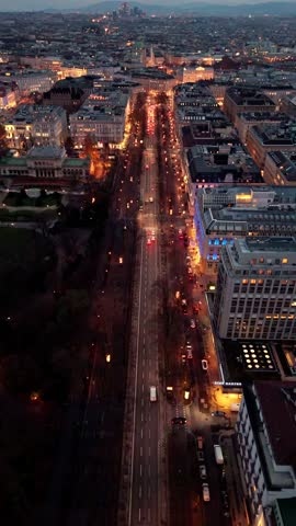 Aerial static drone shot over a Vienna city road at night, showing flowing traffic, illuminated streets, surrounding buildings, winter atmosphere, and glowing city lights across the urban landscape.