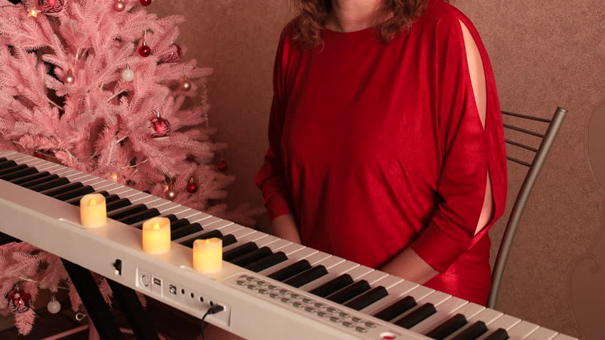 A woman in a red dress is dancing at a white piano next to a pink Christmas tree