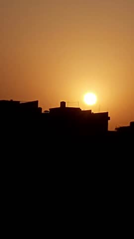 Silhouette of urban rooftops and buildings in Lahore against a vibrant glowing sunset sky, capturing the warm orange hues of dusk over the cityscape in Punjab, Pakistan.