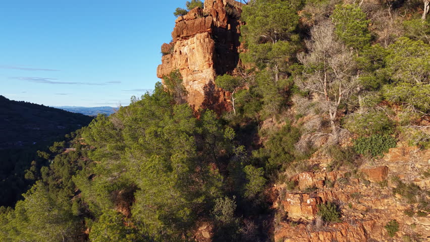 Aerial shot with the camera rising to reveal a scenic viewpoint atop rugged cliffs in the Sierra Calderona Natural Park, Valencia, Spain. Rocky formations and pine forest glow in warm evening light