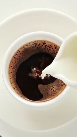 Milk cream is poured into a cup black morning coffee cup. Top view, flat lay. Vertical 