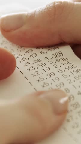 Hands checking grocery receipt or bill after grocery shopping at a supermarket. Expense tracking and home budgeting. Vertical