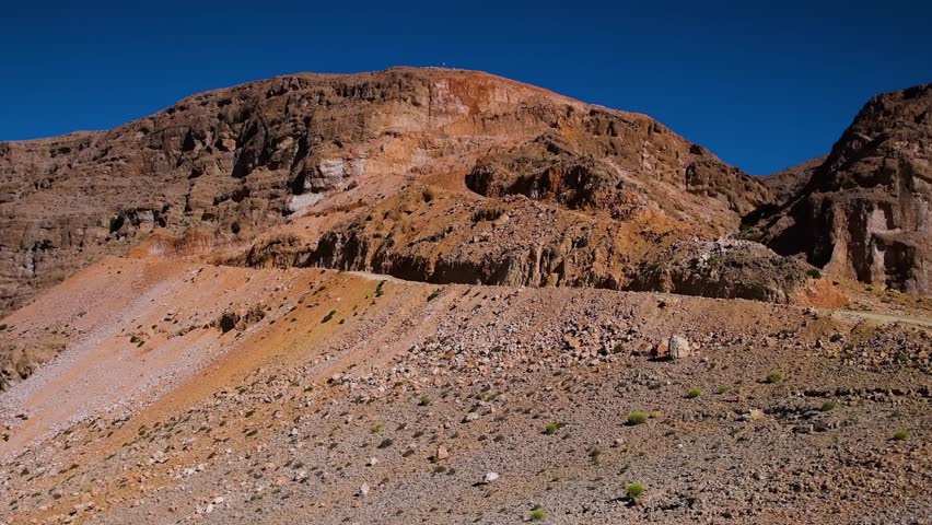 A wide shot of the rugged, arid mountains and valleys of Wadi Shab and the nearby Village Al Fahal in Oman. The landscape features rocky terrain, steep cliffs, and a clear blue sky, capturing the natu