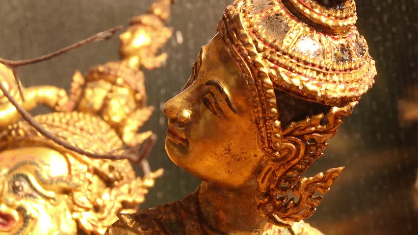 Close up of traditional Thai Khon puppets representing characters from the Ramayana epic. The golden figures are intricately designed and displayed in a glass dome at Arun temple Bangkok, Thailand.