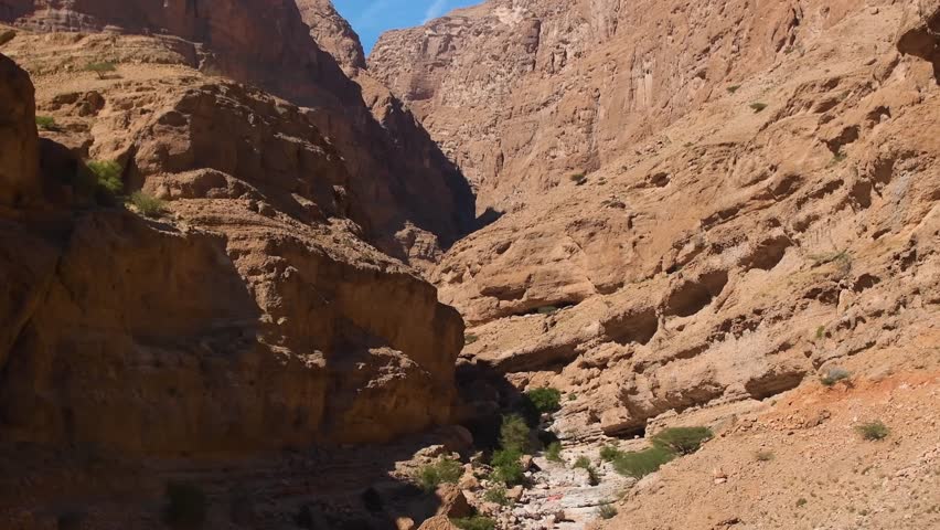 A view of the rugged canyon walls and lush greenery of Wadi Shab, Oman. The footage captures the natural beauty of the valley with its river running through it, leading to hidden pools and waterfalls.