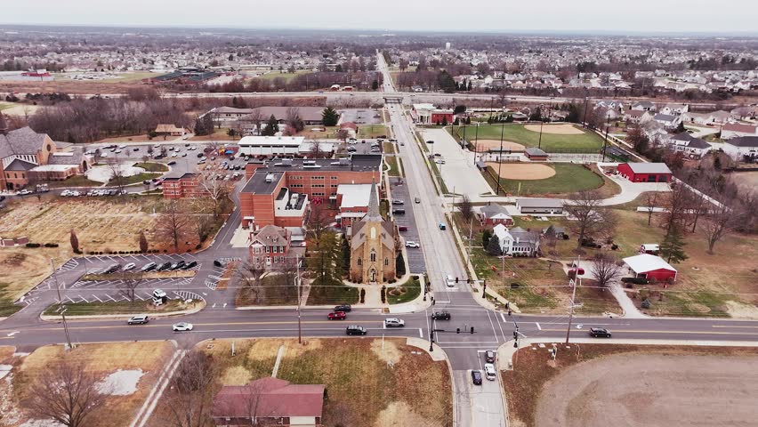 Aerial zoom in from a catholic church steeple to a neighborhood with street traffic and other buildings.