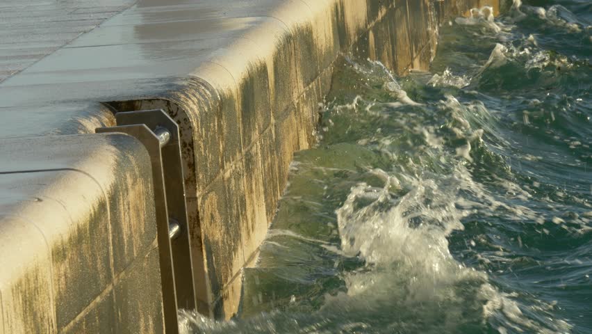 Waves crashing against modern seaside promenade wall in golden sunlight