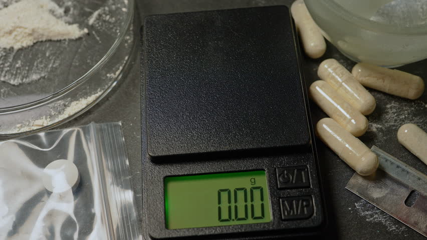 Drug dealer measure powder of synthetic opioid drug of fentanyl in the gelatin capsule for sale on the streets or parties, using electronic scale. Toxic drug crisis and struggle with an addiction.
