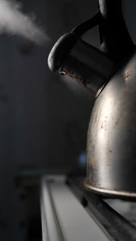 A rusty kettle on the gas stove whistles as water boils inside. Close-up