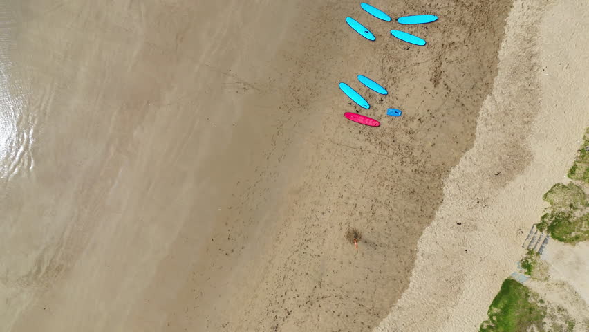 Aerial top-down view of surfers and surfboards near the shoreline as waves break on sandy beach. Minimalist coastal scene with ocean textures, motion patterns and summer seaside atmosphere.