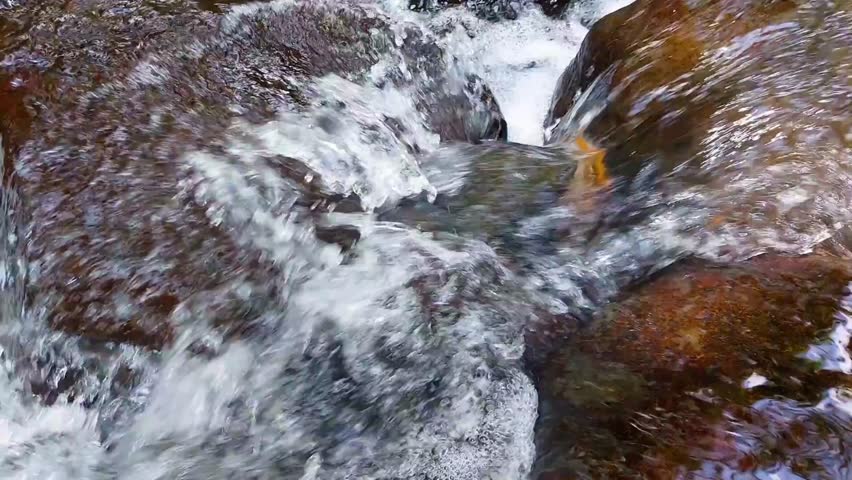 The water appears to ripple and ripple as it passes over various large and small rocks, creating small cascades or waterfalls.