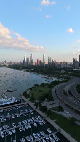 Cinematic aerial view of Chicago Illinois skyline along Lake Michigan with marina and boats, summer light, waterfront curves, calm water, city park and highways framing downtown..
