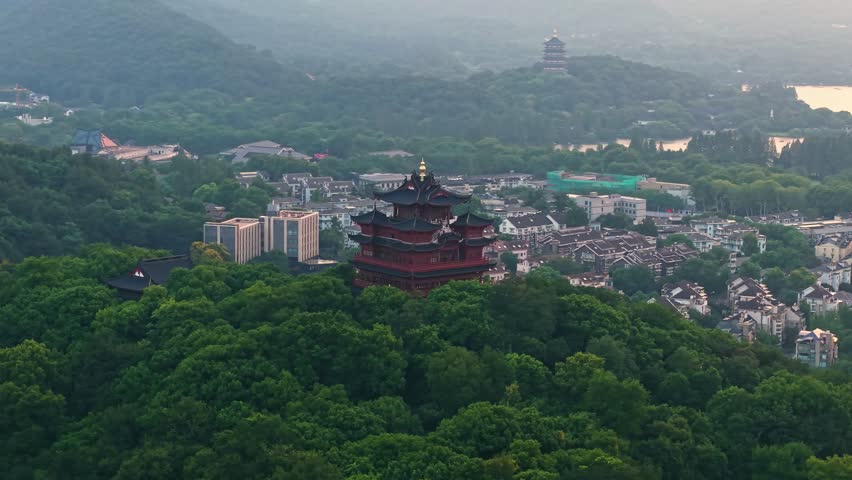 Aerial view of Chenghuang pagoda at sunset over Xihu lake in Hangzhou featuring mountains and lush green trees