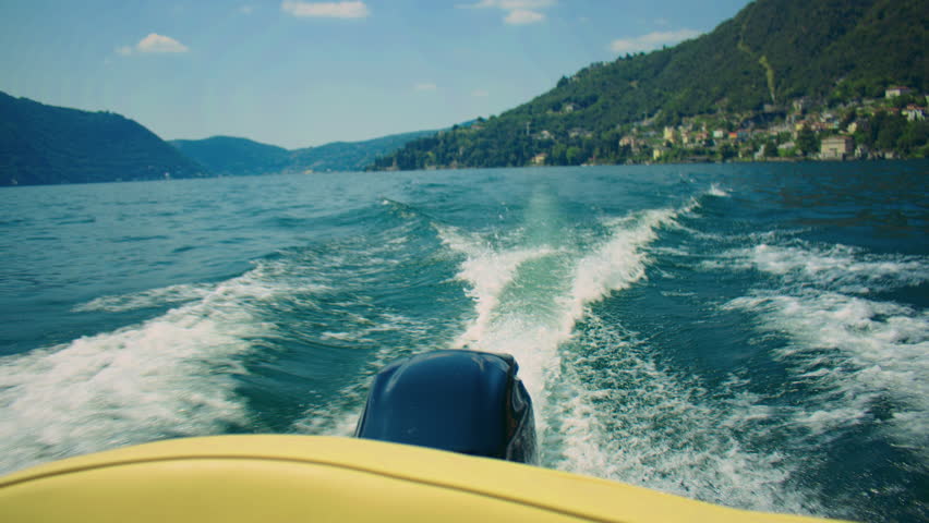 Boat moving across Lake Como leaving wake trails on the water with mountain scenery.
