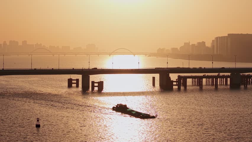 Aerial view of barge travels on Qiantang River under bridges in Hangzhou during golden hour sunset illuminating the water
