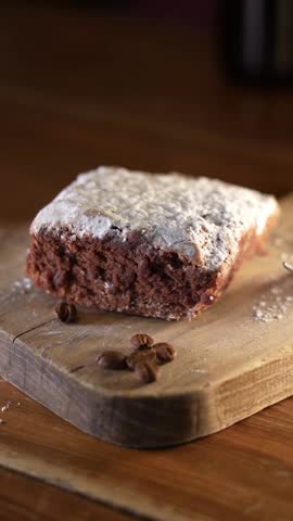 granos de cafe caen frente a un delicioso brownie de chocolate